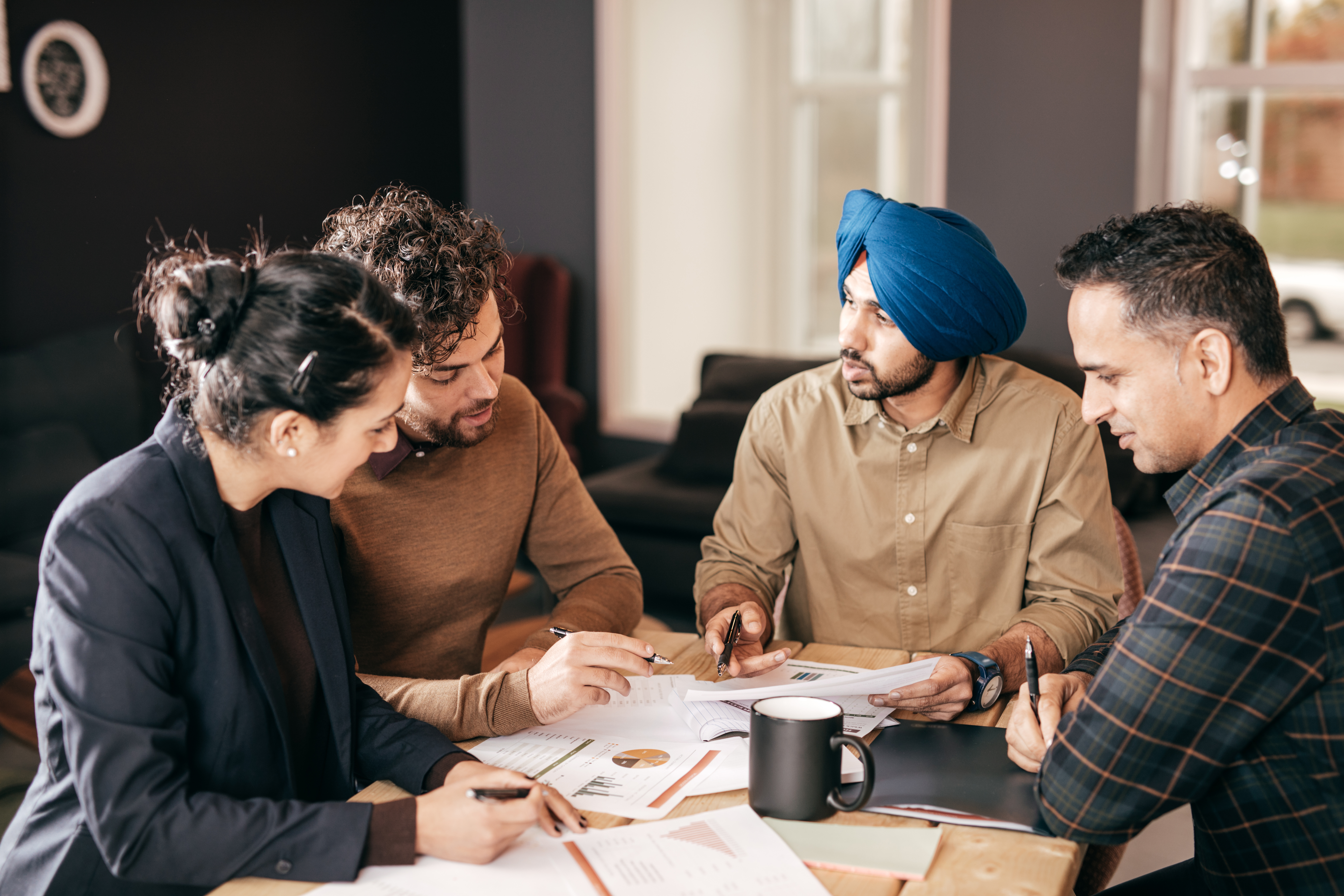 Four people sit at a table with pens in hand, looking at paperwork